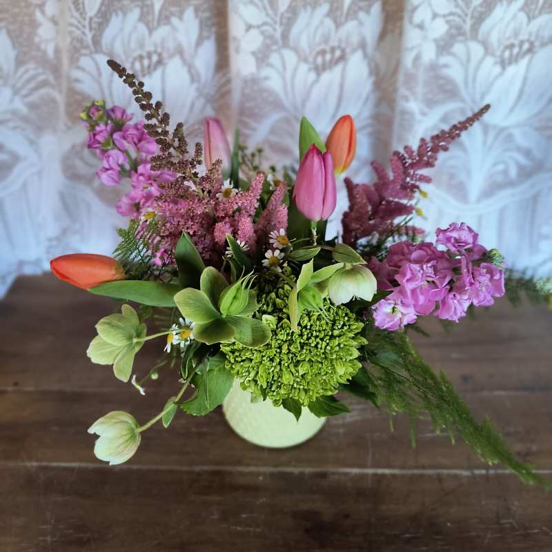 Mixed spring arrangement with pink and orange tulips and green hydrangea in a pale vase