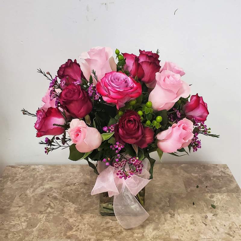 Pink and burgundy roses in a glass vase with a pink ribbon