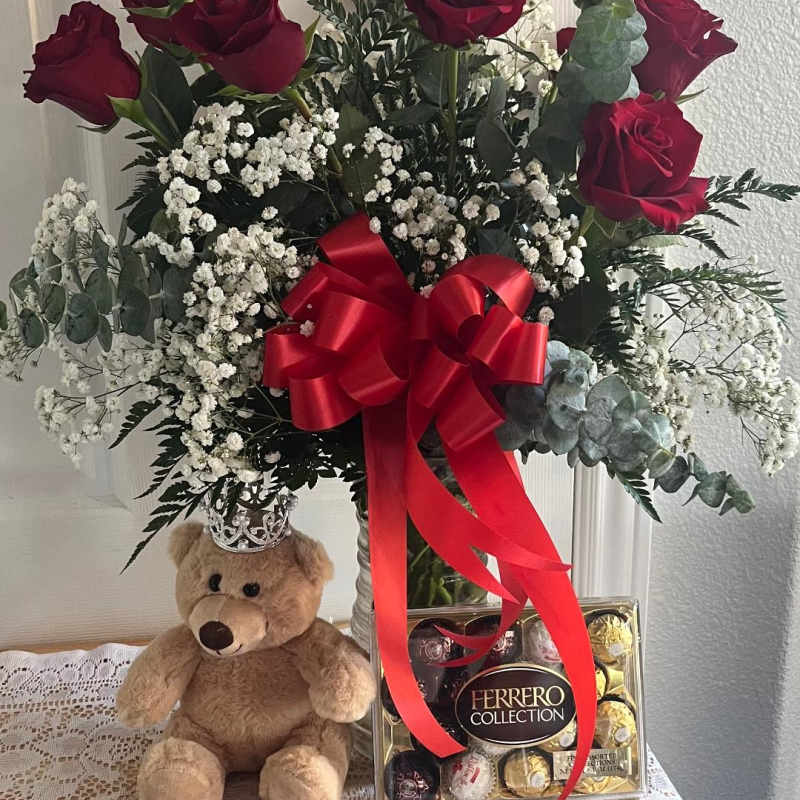 Red roses in a vase with baby’s breath, a teddy bear, and chocolates