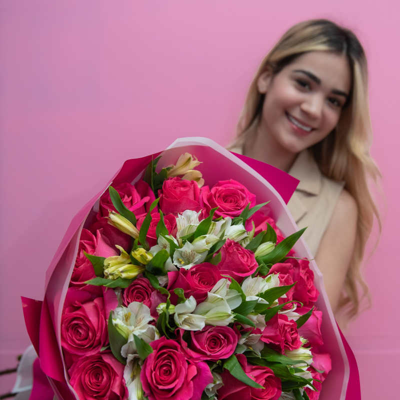 Woman holding a bouquet of pink roses and white flowers wrapped in pink paper