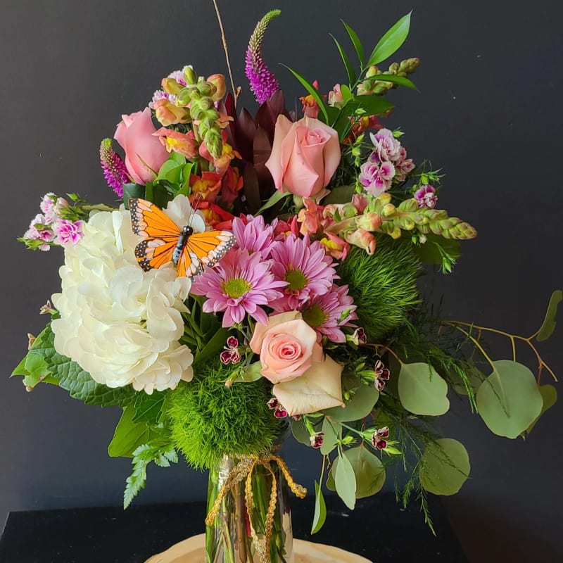 Mixed bouquet in a glass vase with pink roses, white hydrangea, and a butterfly pick