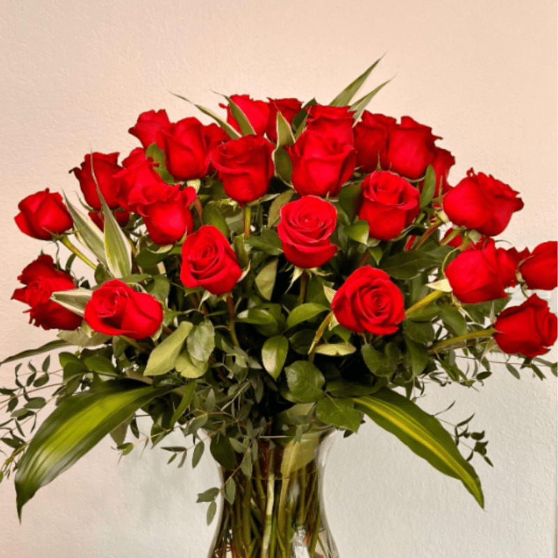 Red roses arranged in a clear glass vase with greenery