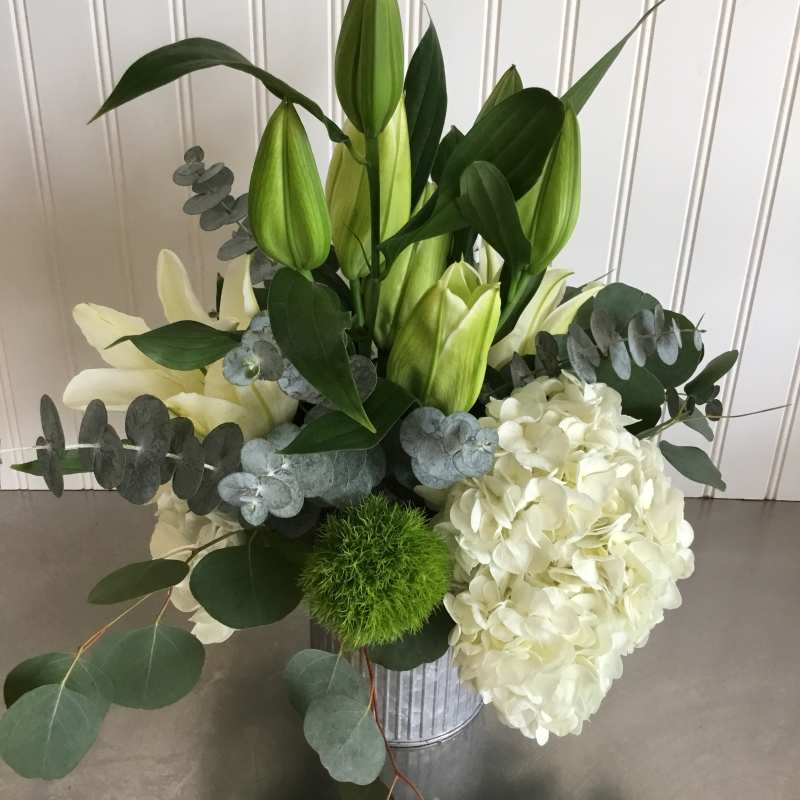Arrangement of white hydrangea and lilies with green buds in a metal vase