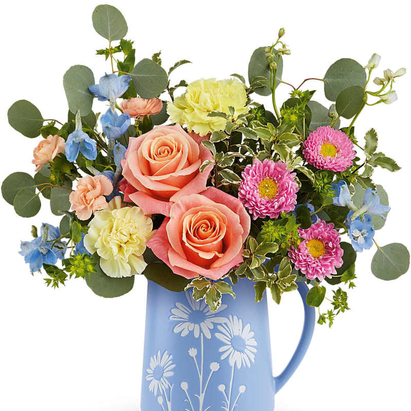 Mixed bouquet of peach roses, yellow carnations and blue blooms in a blue daisy-print pitcher