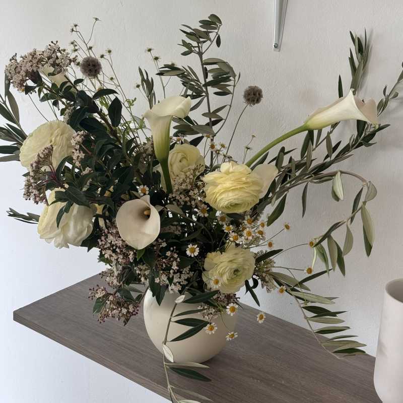 White floral arrangement in a cream vase with calla lilies and ranunculus