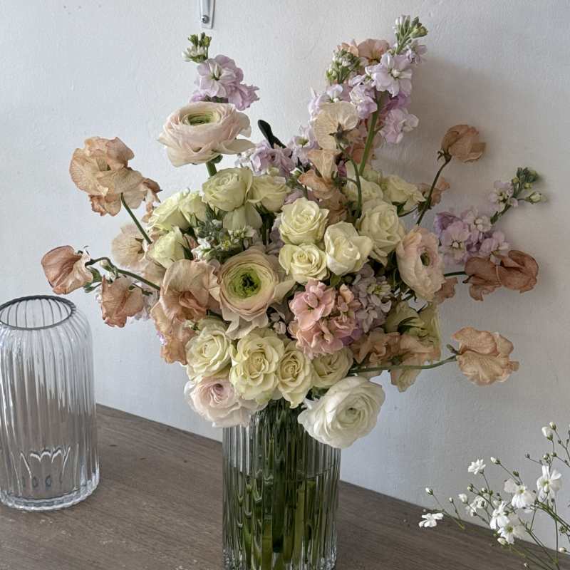 Pastel bouquet of roses and ranunculus in a ribbed glass vase