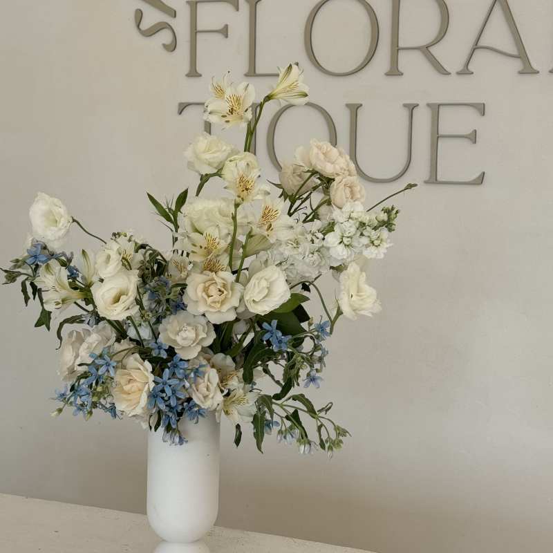Tall white floral arrangement in a white vase with blue accents