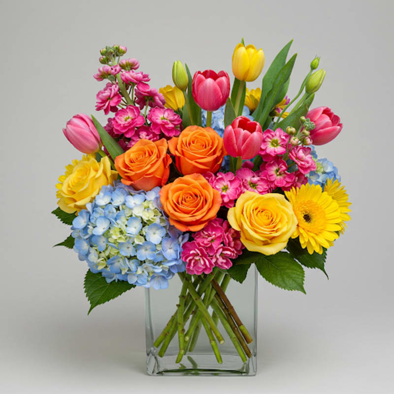 Mixed bouquet in a clear glass vase with roses, tulips, hydrangea, and daisies