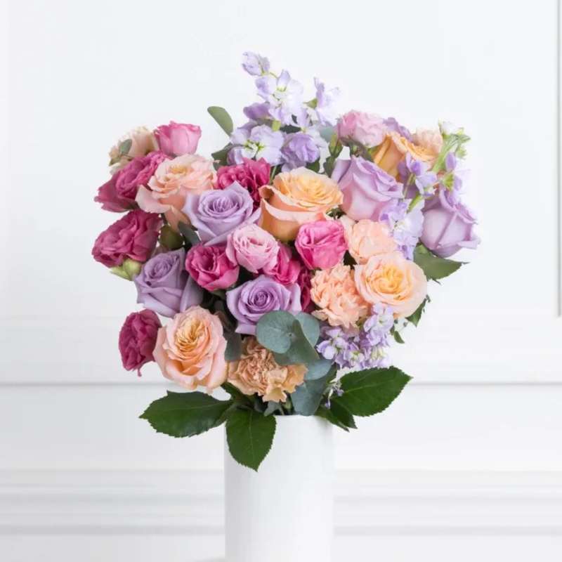 Bouquet of pastel roses and lavender flowers in a white vase