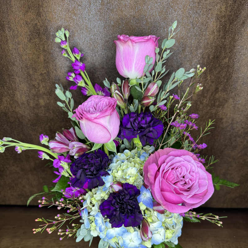 Pink roses and purple flowers in a clear glass vase