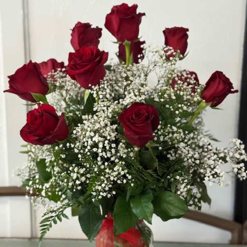 Red roses arranged with white baby's breath in a clear glass vase.