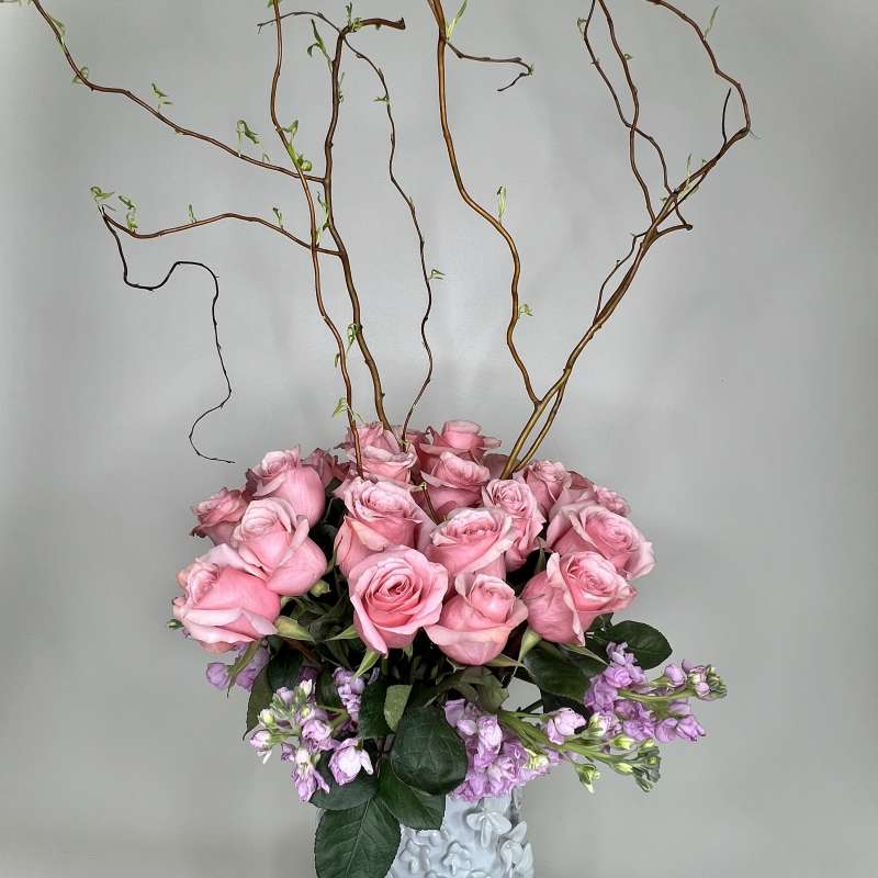 Pink roses in a white vase with tall curly branches