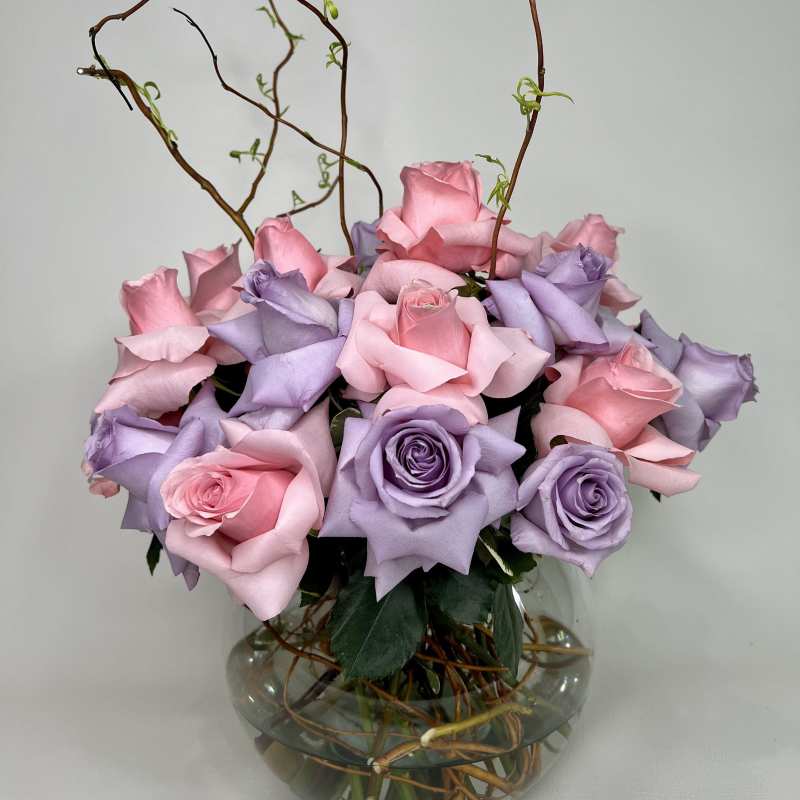 Pink and lavender roses arranged in a round glass vase with curly branches