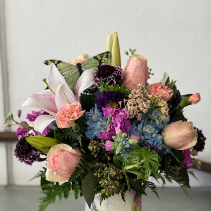 Mixed bouquet with lilies, roses, hydrangeas, and a butterfly accent in a floral vase