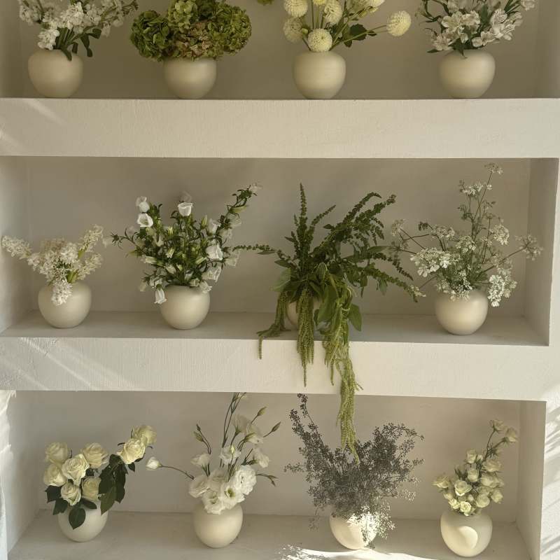 Shelved display of small white floral arrangements in cream vases