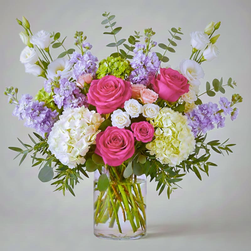 Bouquet of pink roses, white blooms, and lavender flowers in a clear glass vase