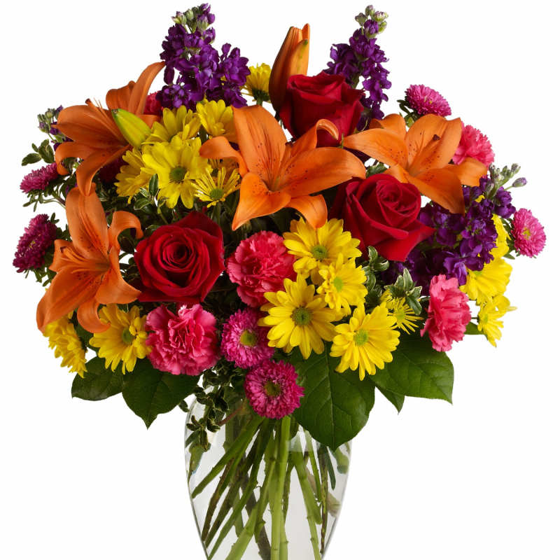 Mixed bouquet of orange lilies, red roses, and yellow daisies in a glass vase