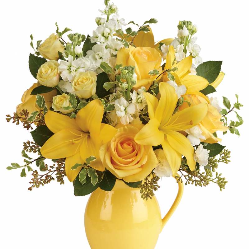 Yellow roses and lilies arranged in a yellow pitcher vase