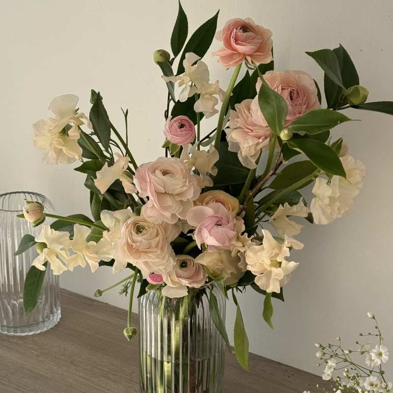 Blush pink ranunculus and white sweet pea in a clear glass vase