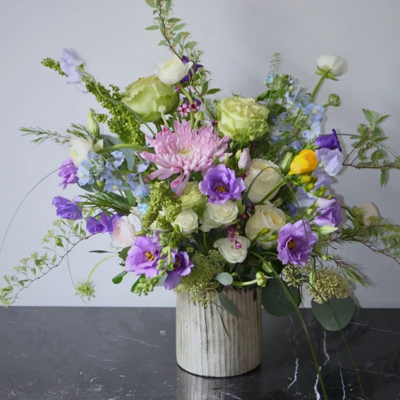 Mixed floral arrangement in a ribbed white vase with purple, white, and green blooms