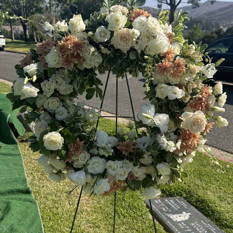 Large floral wreath of white and peach flowers on a stand outdoors