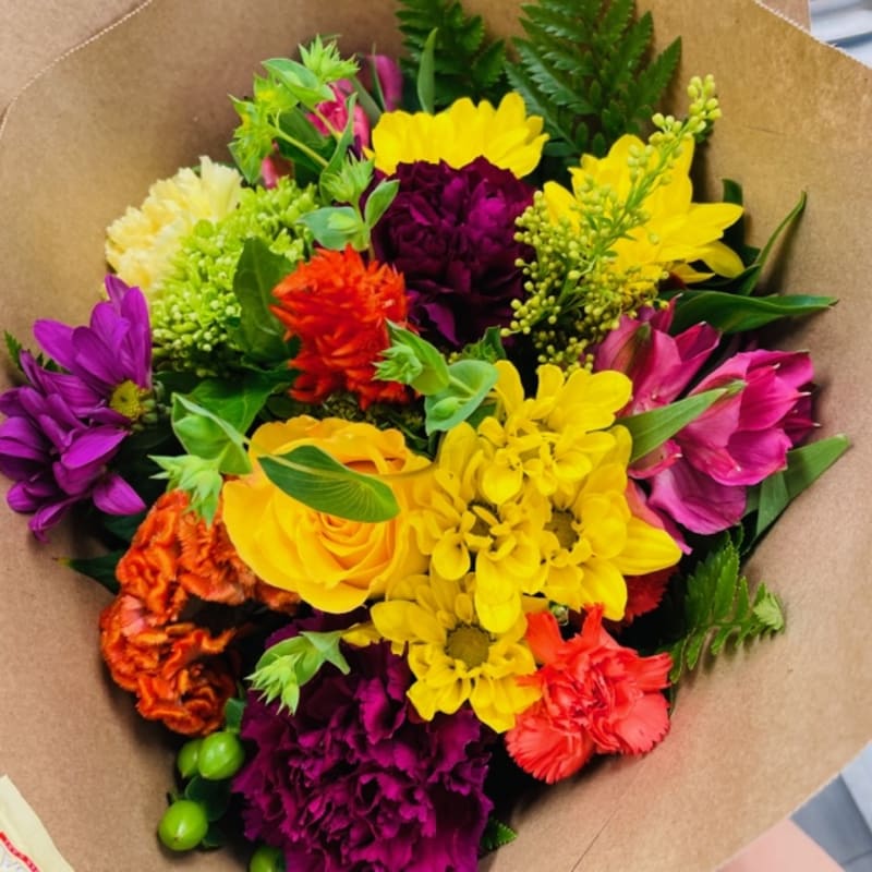 Colorful mixed bouquet with yellow, purple, pink, and orange flowers wrapped in brown paper