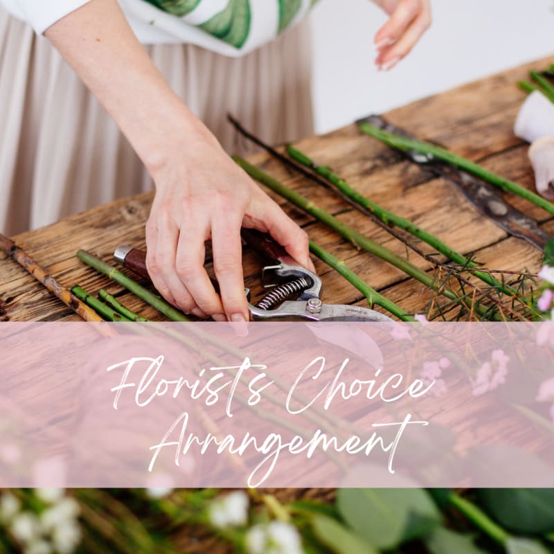 Person trimming flower stems on a wooden table with floral tools