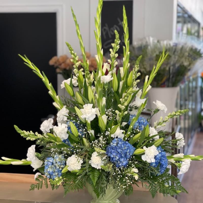 Tall blue and white floral arrangement in a pale green vase