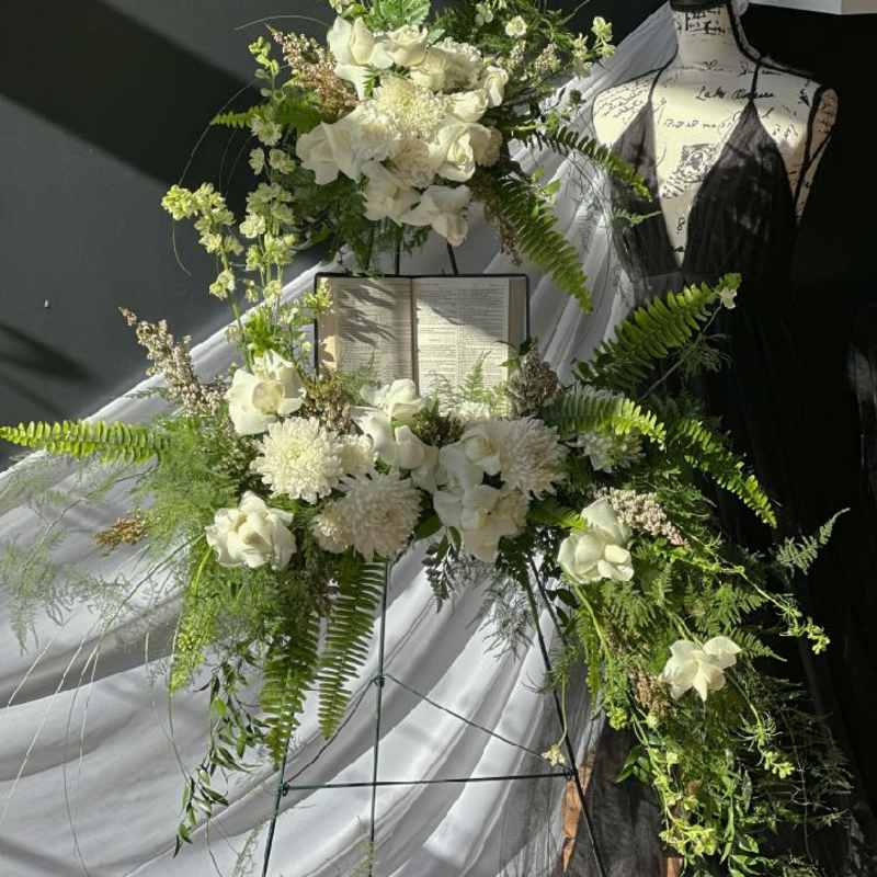 White floral standing spray on an easel beside a mannequin and draped fabric