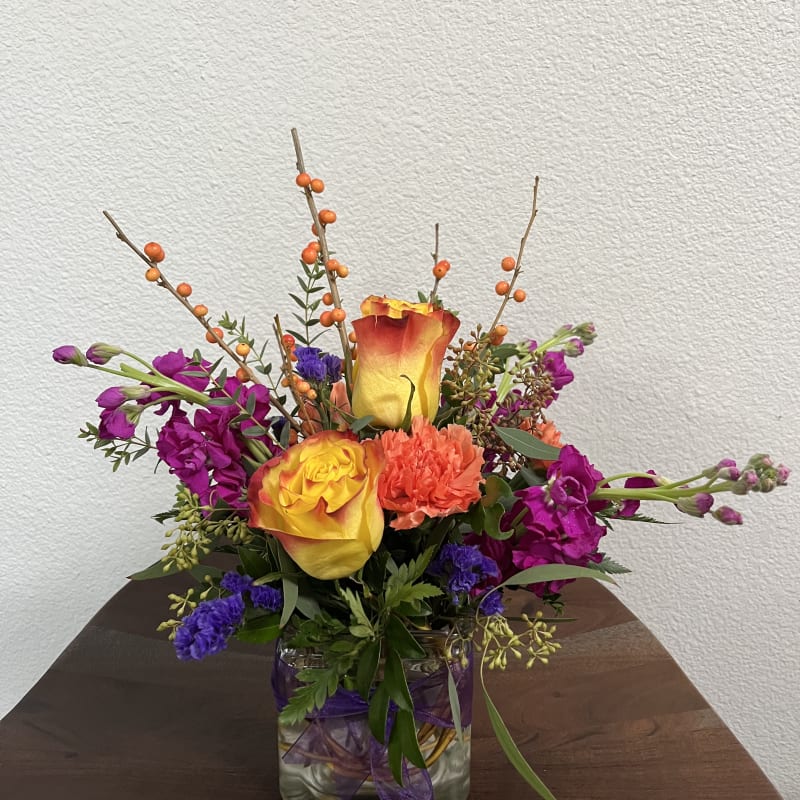 Mixed bouquet in a glass vase with yellow-orange roses and purple flowers
