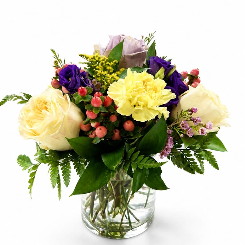 Mixed bouquet of cream, yellow, and purple flowers in a glass vase