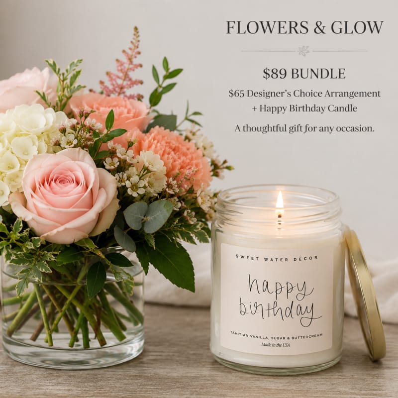 Pink and white flower arrangement in a glass vase beside a lit birthday candle.