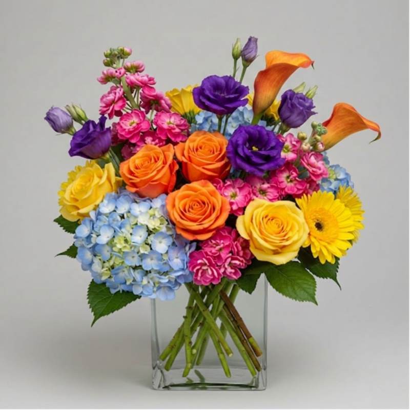 Colorful bouquet in a clear glass vase with roses, hydrangea, calla lilies, and daisies