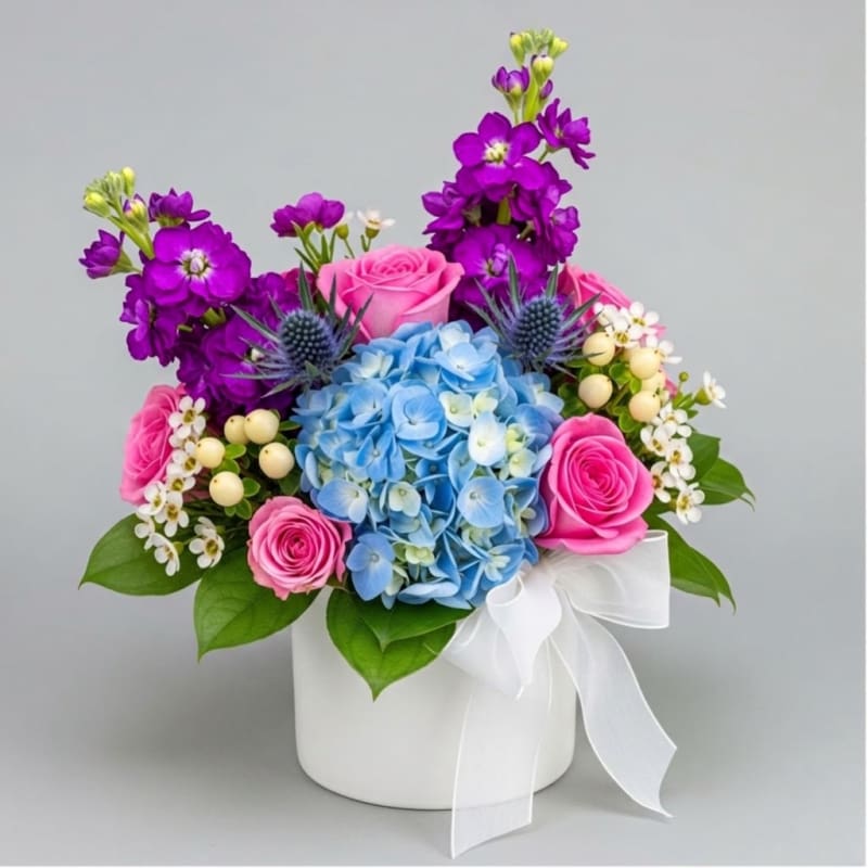 Pink roses and blue hydrangea in a white hatbox with a ribbon