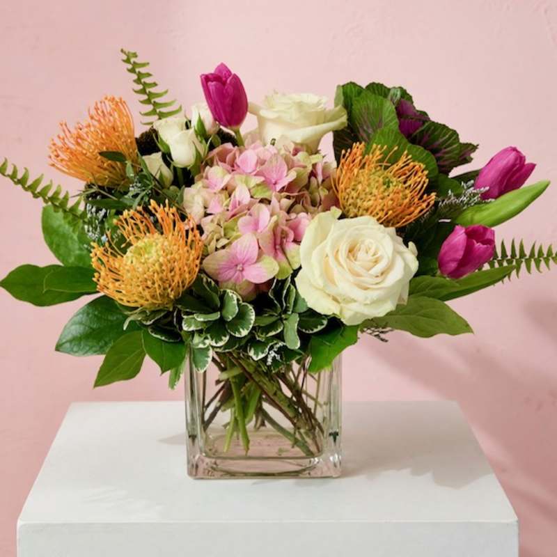 Mixed bouquet of pink, white, and orange flowers in a clear glass vase