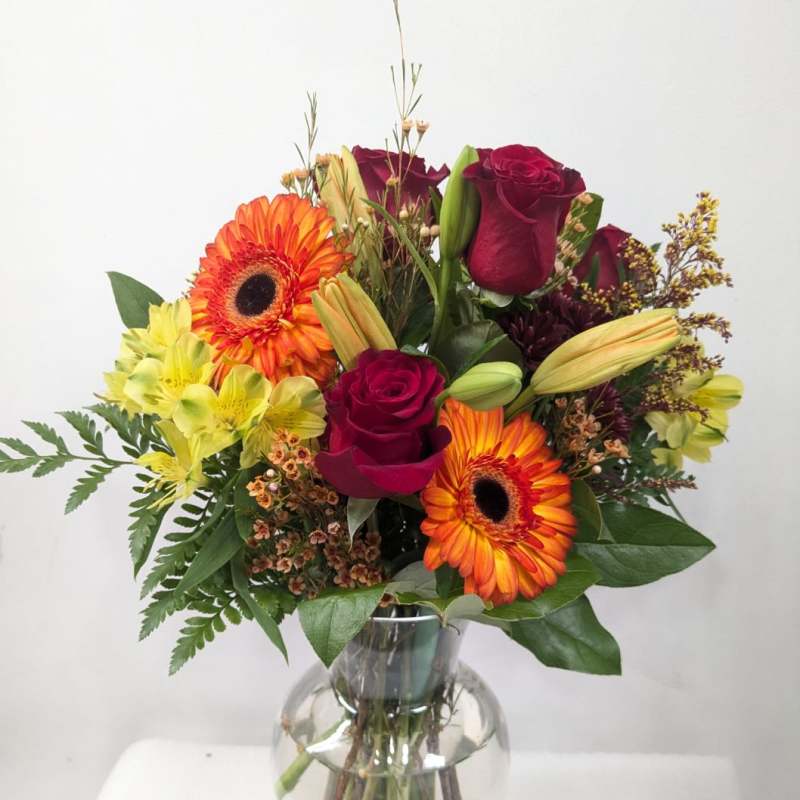 Bouquet of red roses, orange gerbera daisies, and yellow alstroemeria in a glass vase