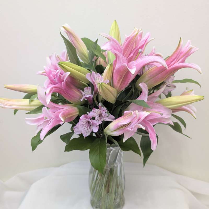 Pink lilies in a clear glass vase with small lavender flowers