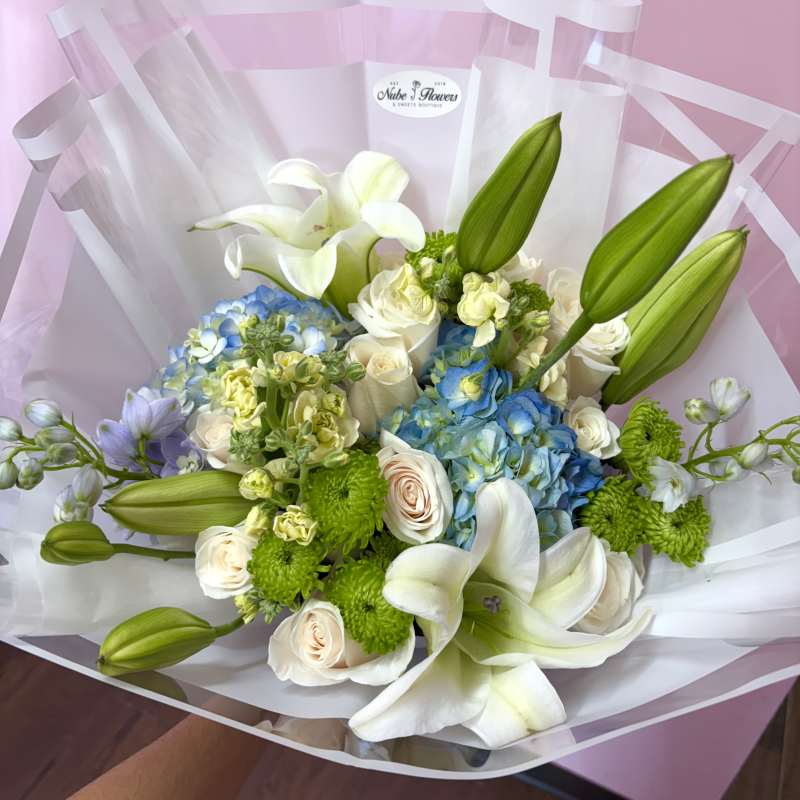 Bouquet of white lilies, blue hydrangeas, and cream roses wrapped in clear paper