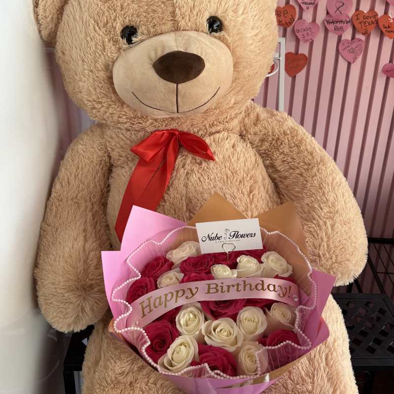 Large teddy bear holding a bouquet of pink and white roses