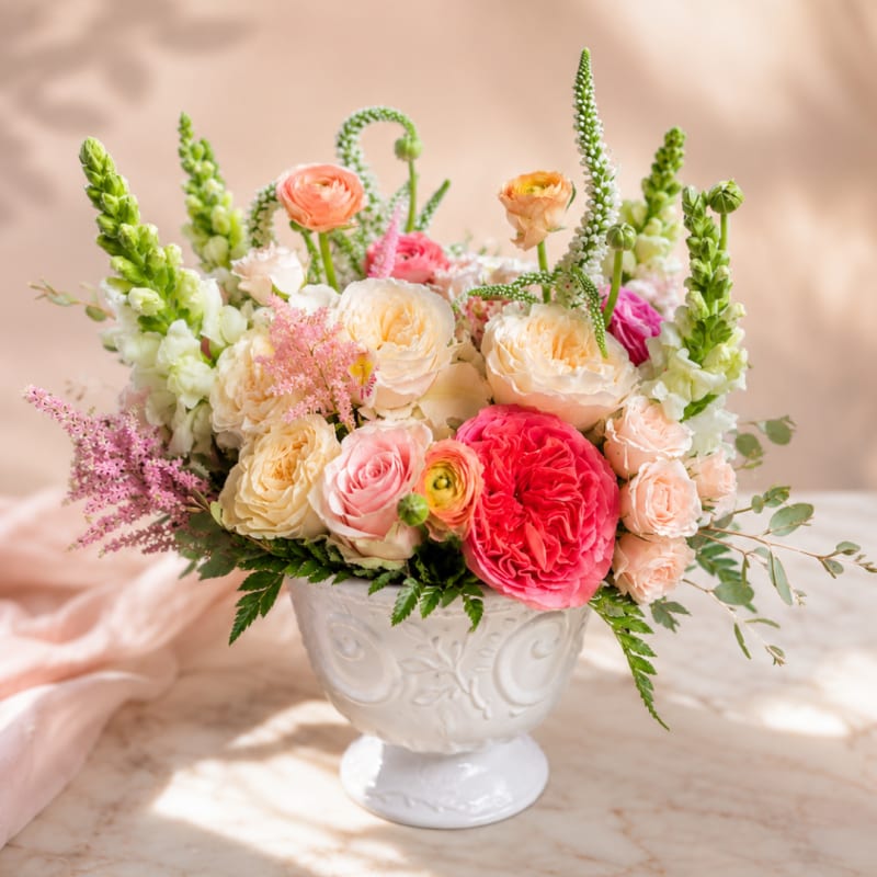 Mixed pastel flower arrangement in a white pedestal vase