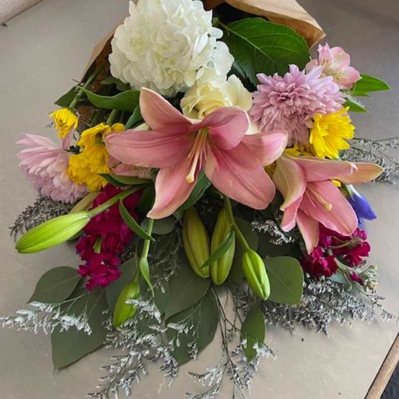 Bouquet of pink lilies, white hydrangea, and mixed blooms wrapped in brown paper