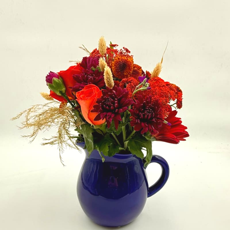 Red and orange flowers arranged in a blue pitcher vase