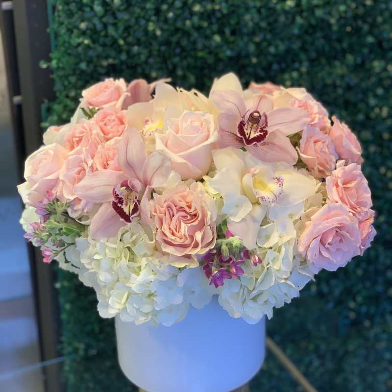 Pink roses and orchids arranged in a white hat box