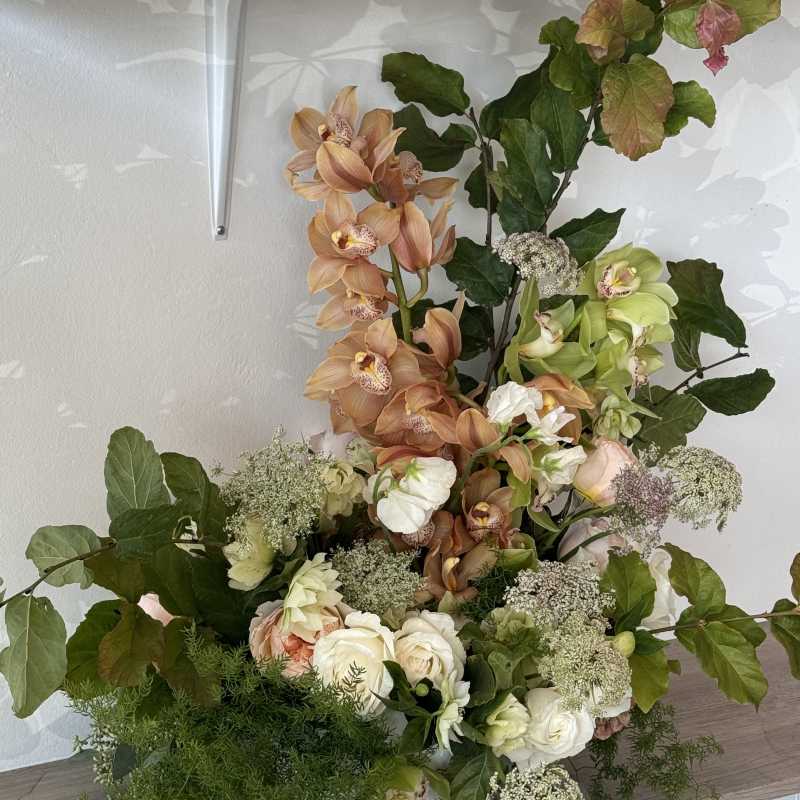 Tall floral arrangement with peach orchids, white roses, and greenery