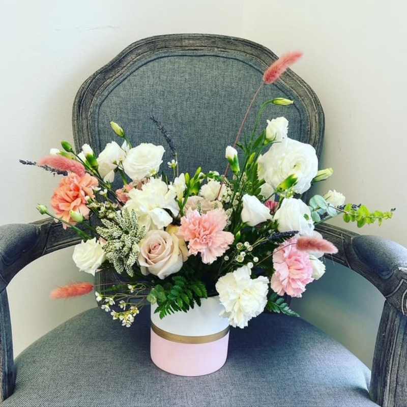Mixed bouquet of white and blush flowers in a pink-and-white box.