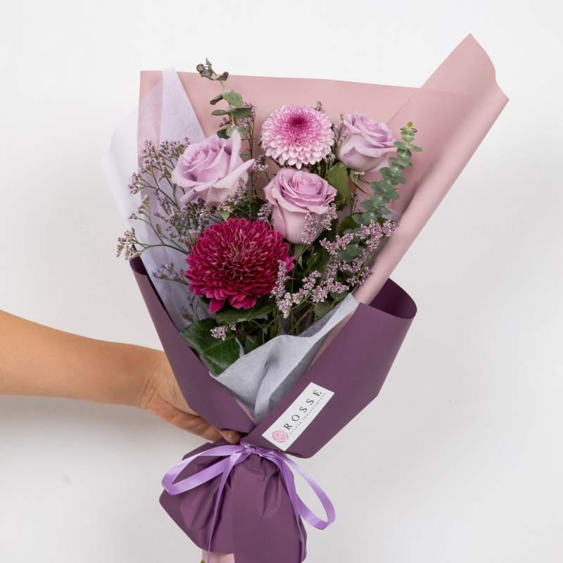 Handheld bouquet of pink roses and chrysanthemums wrapped in purple paper