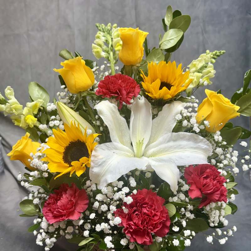 Basket arrangement with white lily, yellow roses, sunflowers, and red carnations