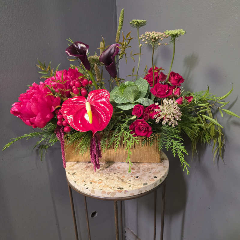Bright pink floral arrangement with roses, calla lilies, and anthurium in a gold box
