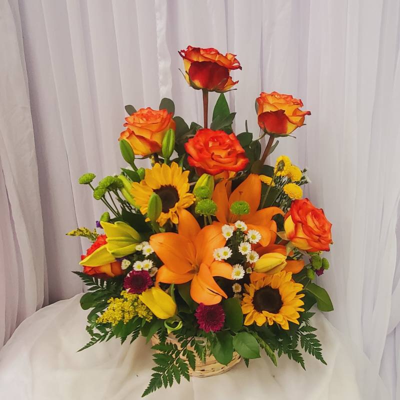Mixed bouquet of orange roses, lilies, and sunflowers in a basket