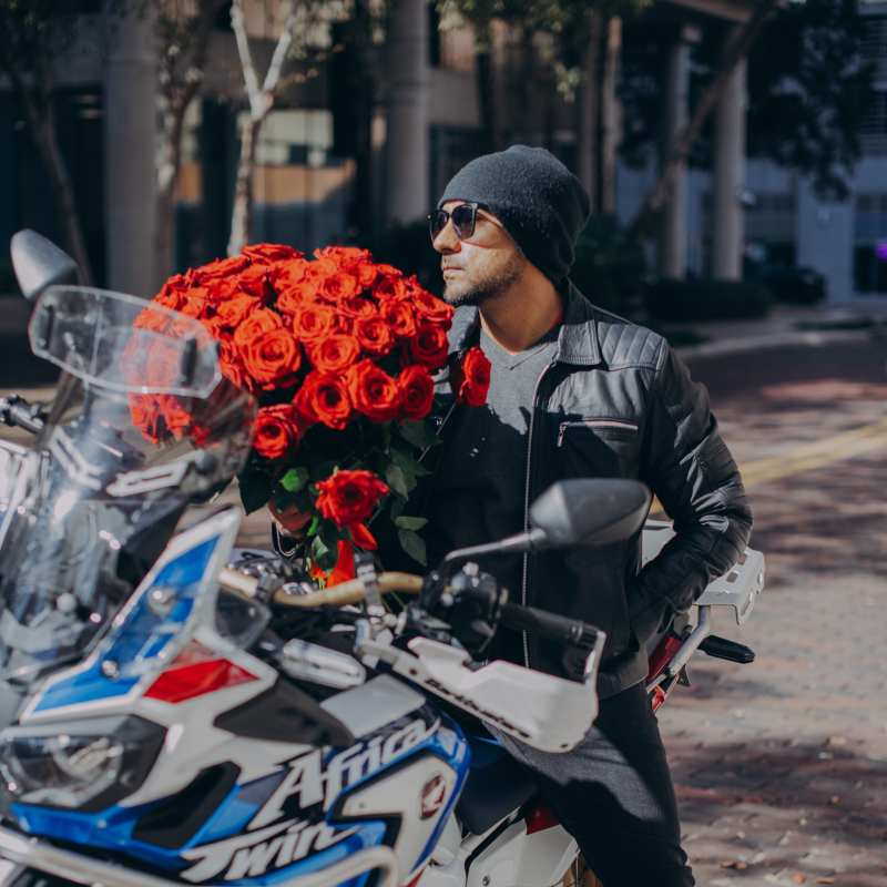 Man on a motorcycle holding a large bouquet of red roses